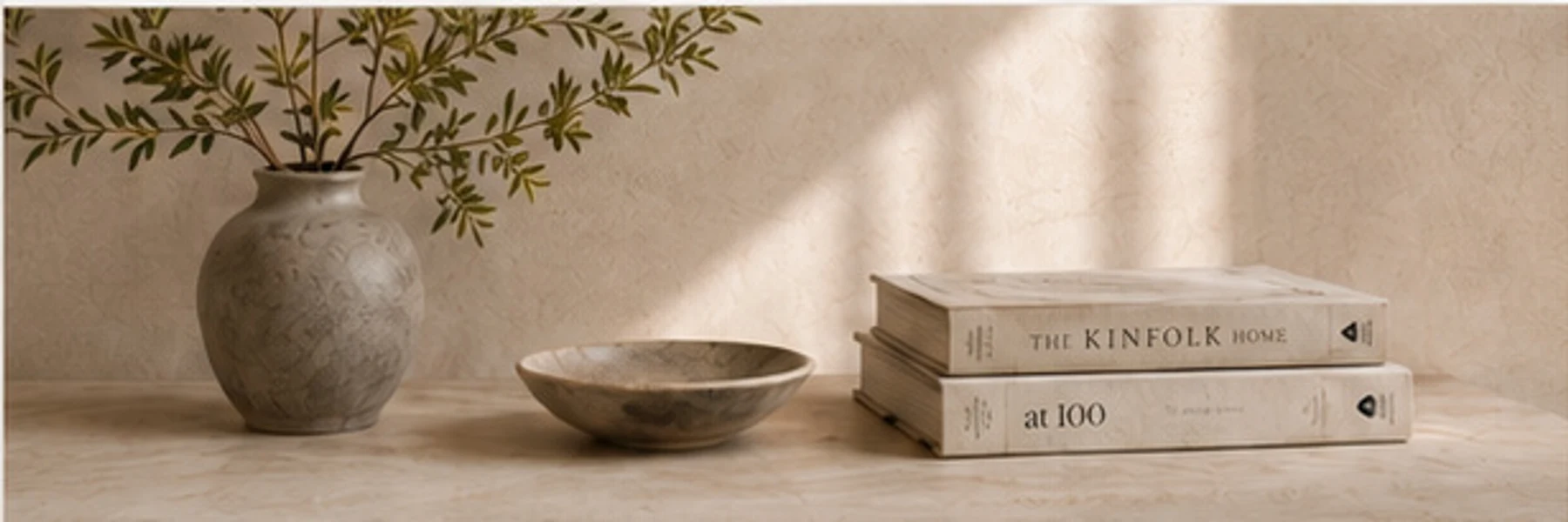 Ceramic vase, bowl and books on a warm stone shelf in soft light